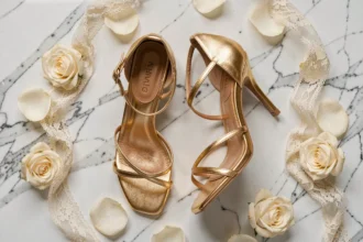 Chaussures dorées à talons aiguilles pour témoin de mariage posées sur marbre blanc avec pétales de roses ivoire